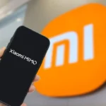 Photograph shows a smartphone with the Xiaomi MiMo app with the orange logo in the background