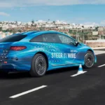 Photograph shows a blue color Mercedes EQS equipped with steer-by-wire technology driving on a road