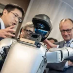 Photograph shows Unitree founder Wang Xingxing (left) introducing a robot to German Chancellor Friedrich Merz in February 2026
