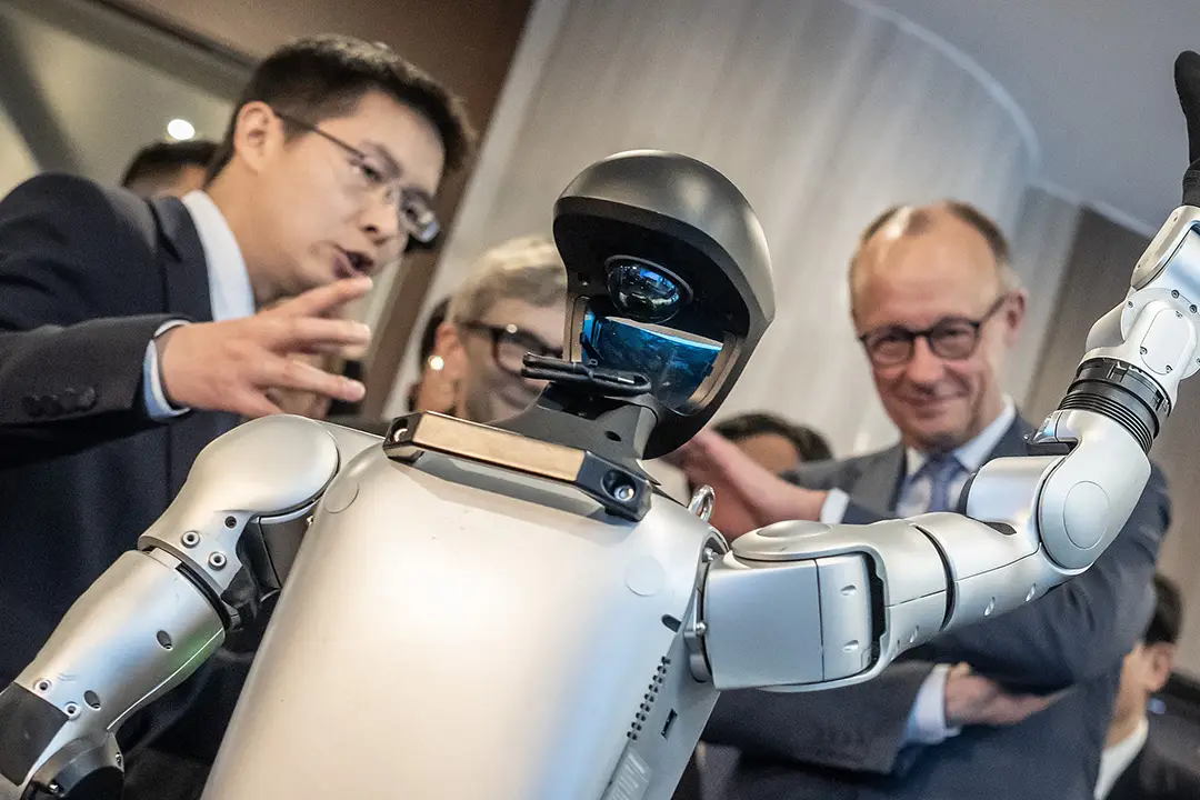 Photograph shows Unitree founder Wang Xingxing (left) introducing a robot to German Chancellor Friedrich Merz in February 2026