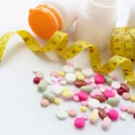 Photograph shows a range of weight-loss pills in the foreground with a measuring tape in the background